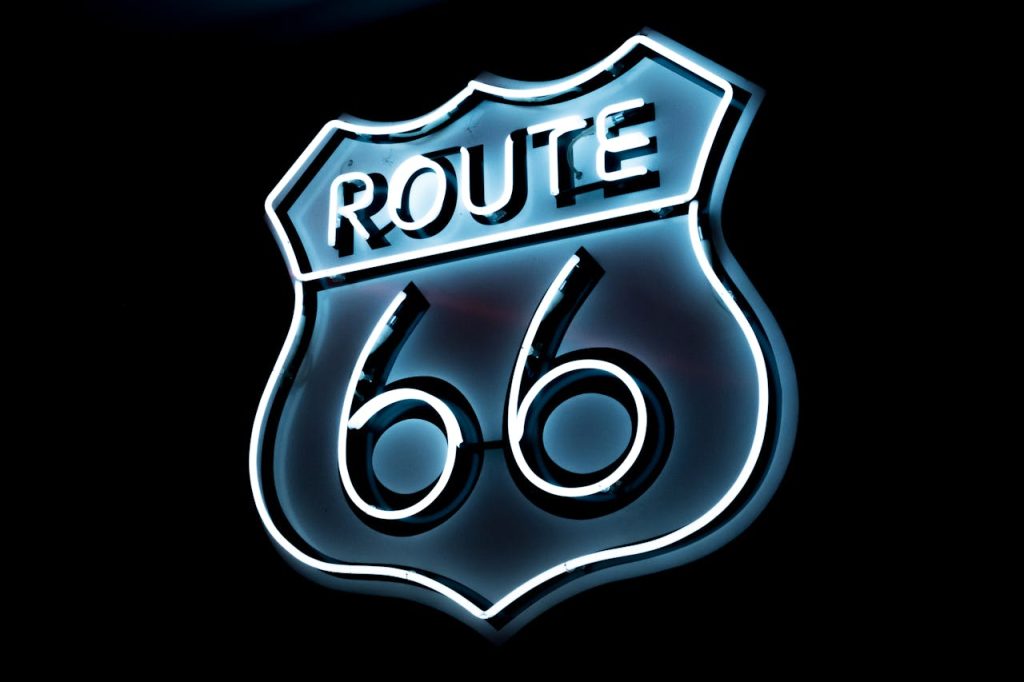 Bright neon Route 66 sign glowing on a black background, vintage style.